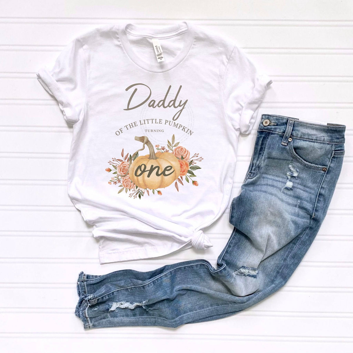 White Daddy of the Little Pumpkin tee laid flat beside jeans.