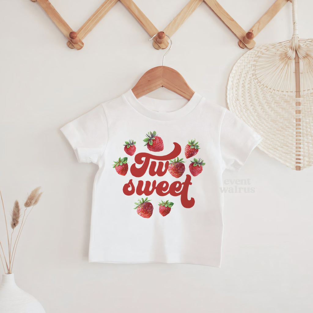 White strawberry Two Sweet baby tee hanging on a wooden peg rail.
