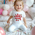 Smiling toddler girl among pink balloons in a white strawberry Two Sweet tee.