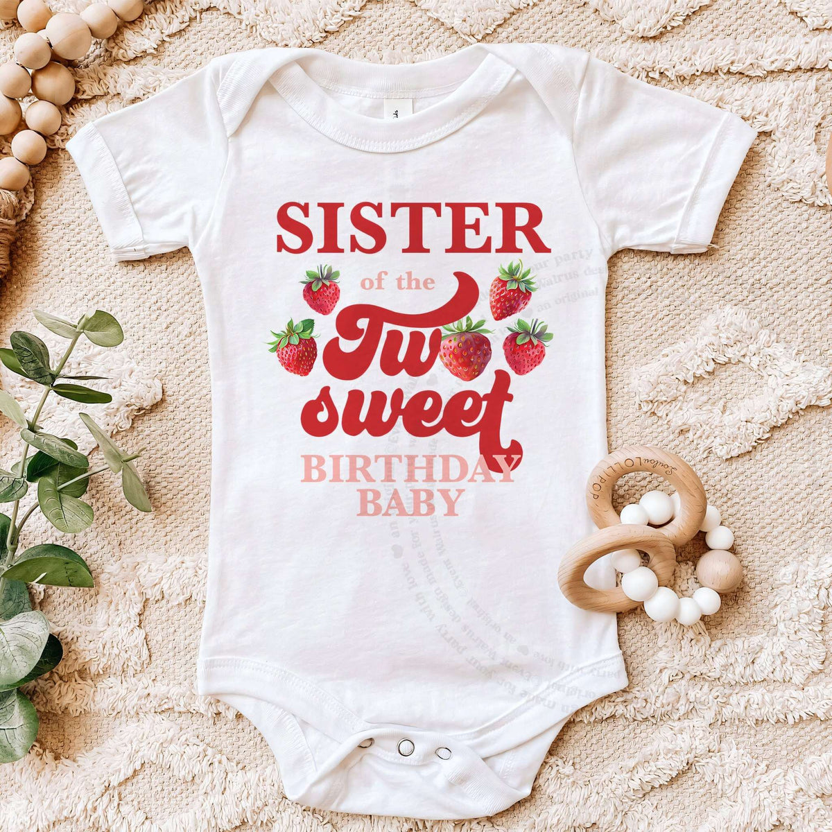 White Sister of the Two Sweet bodysuit on a beige blanket with a wooden teether.