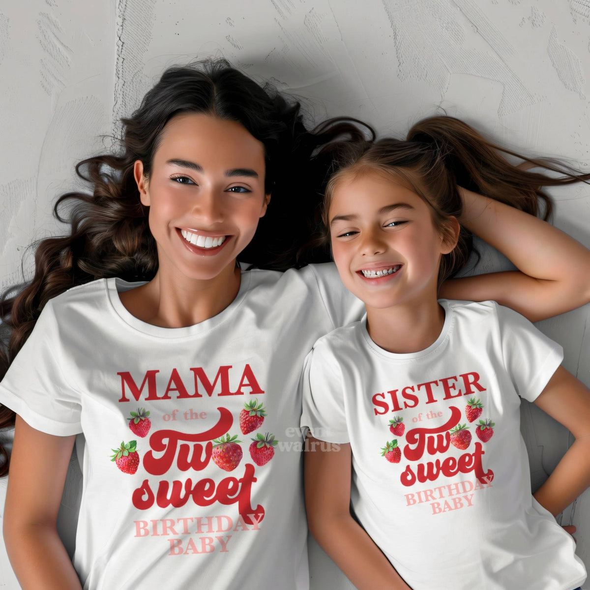 Little girl lying beside her mom in white Sister and Mama strawberry shirts.