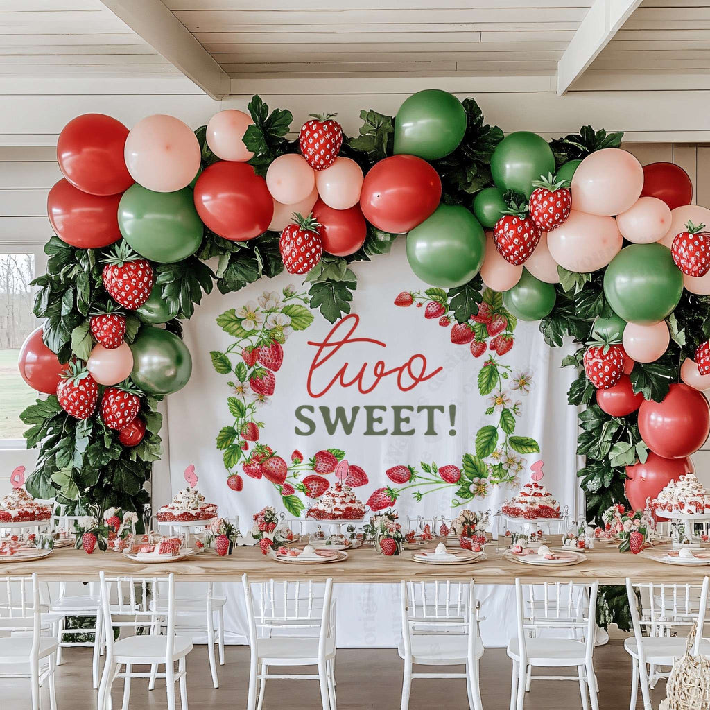 Two sweet strawberry vine backdrop above a long party table with red and green balloons.