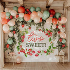 Strawberry two sweet backdrop under a wooden pergola with peach, coral and green balloons.