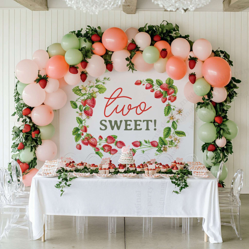Two sweet strawberry backdrop behind a white dessert table with a coral and sage balloon arch.