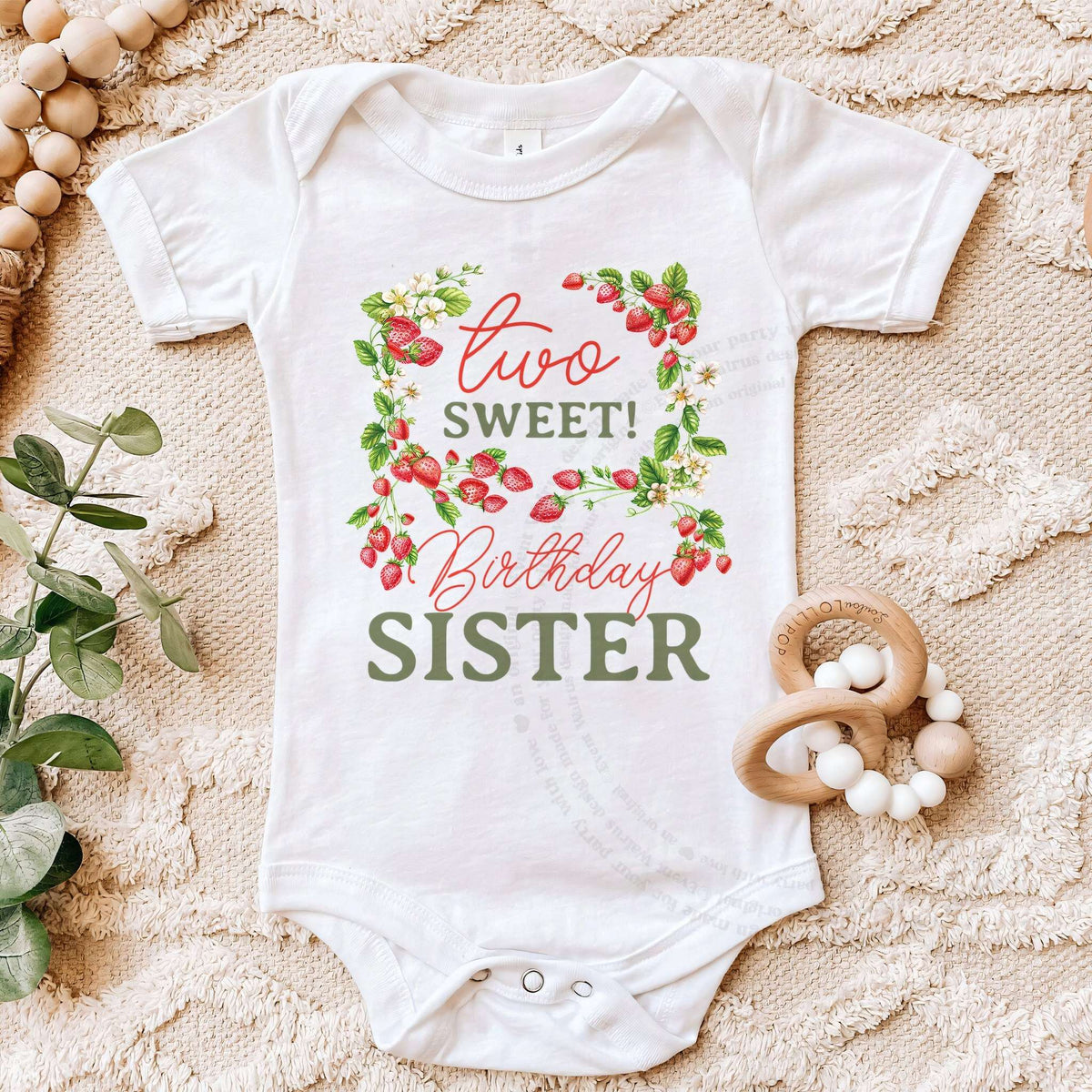 White Two Sweet Birthday Sister bodysuit on a beige blanket with a wooden teether.