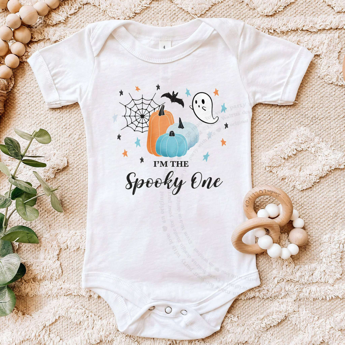 White I'm the Spooky One bodysuit on a beige blanket with a wooden teether.