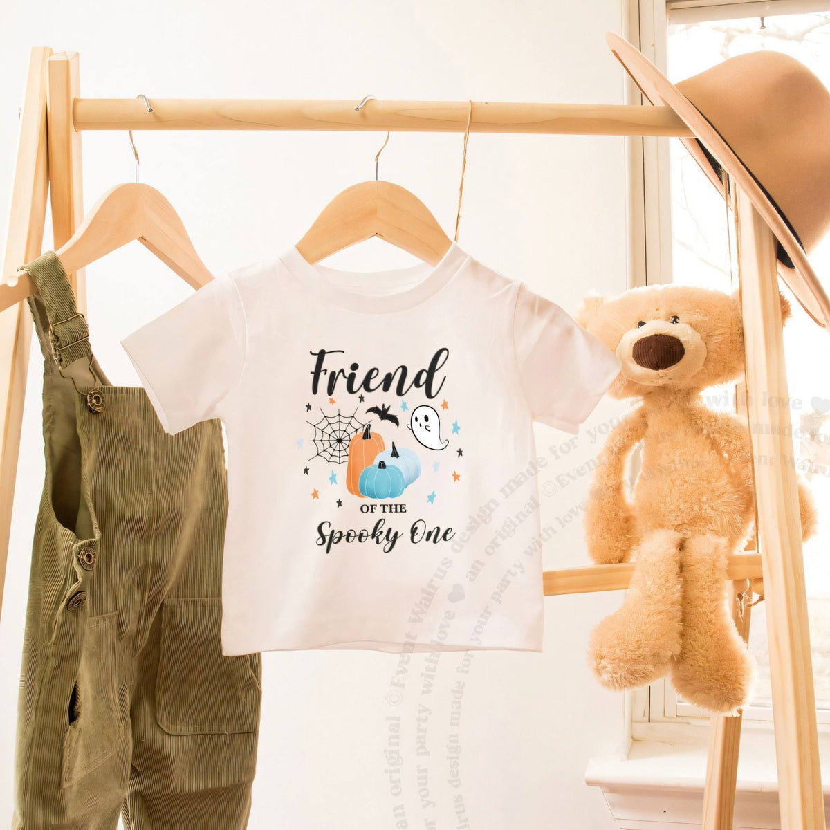 White Friend of the Spooky One toddler tee on a wooden clothes rack beside a teddy bear.