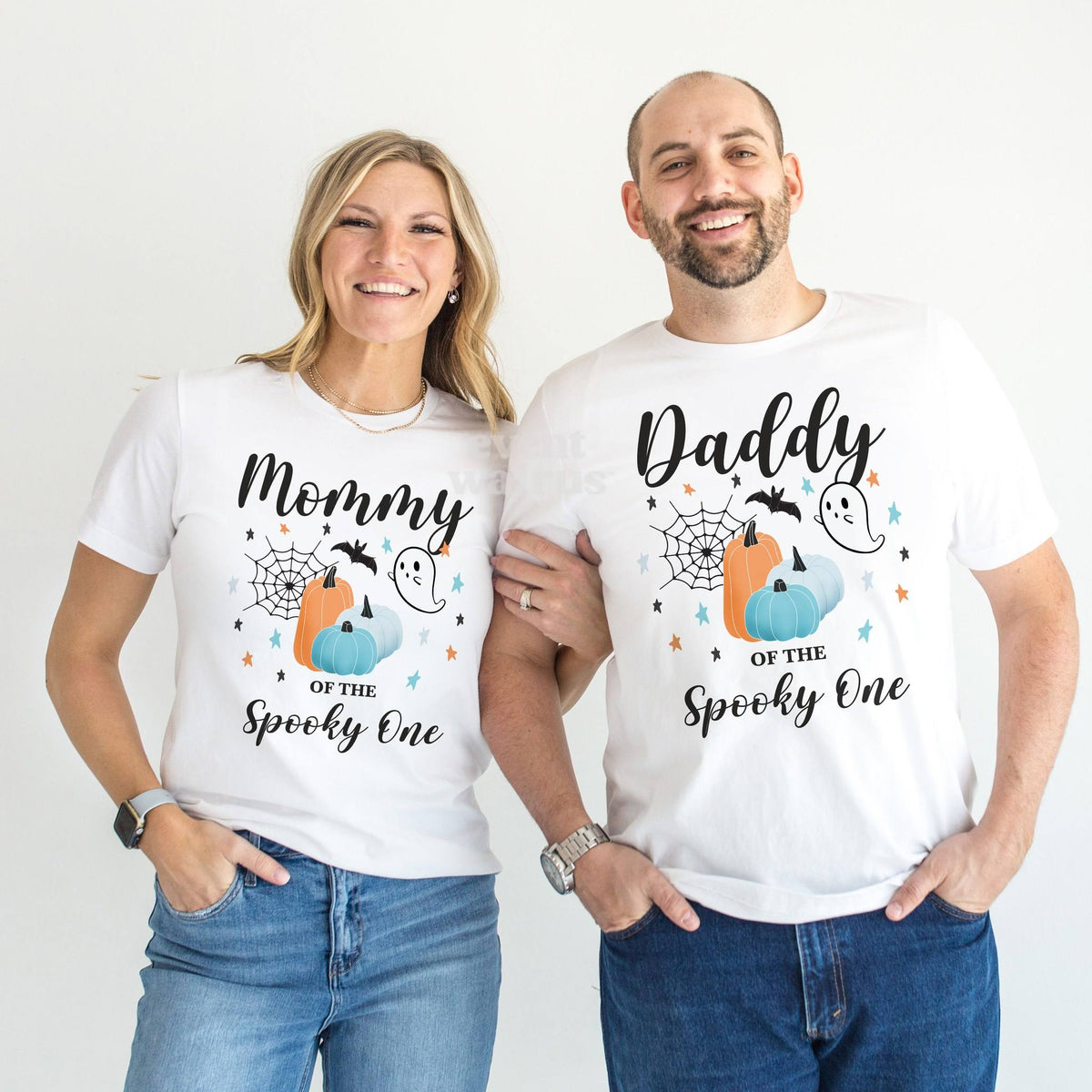 Mom and Dad standing together in white Mommy and Daddy teal pumpkin Spooky One shirts.