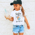Girl in a ball cap holding a drink in a white Sister of the Spooky One shirt.