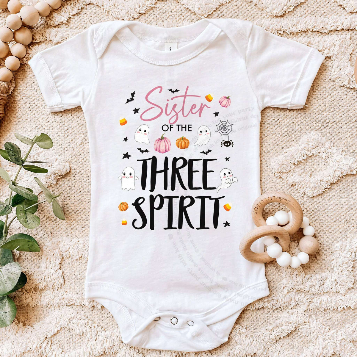 White Sister of the Three Spirit bodysuit on a beige blanket with a wooden teether.