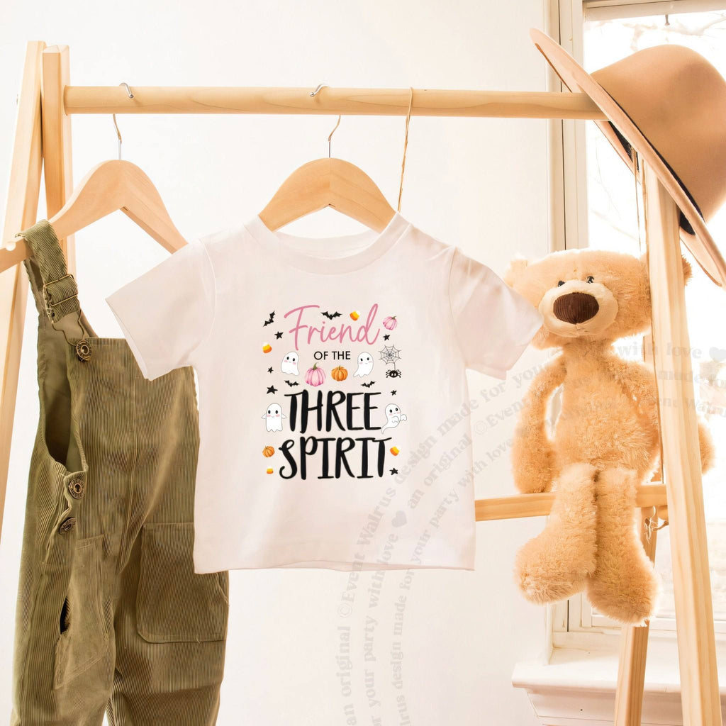 White Friend of the Three Spirit toddler tee on a wooden clothes rack beside a teddy bear.