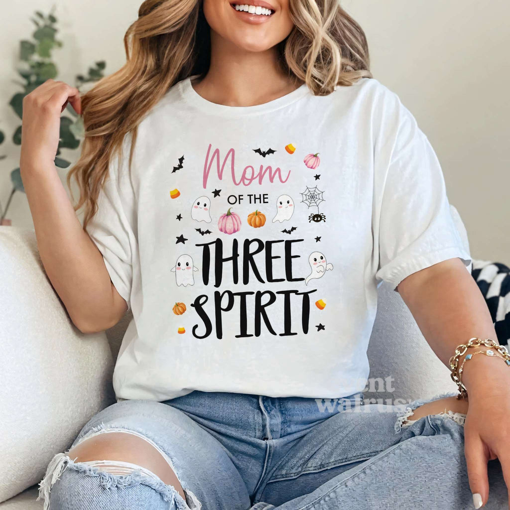 Woman sitting on a sofa in a white Mom of the Three Spirit Halloween shirt.