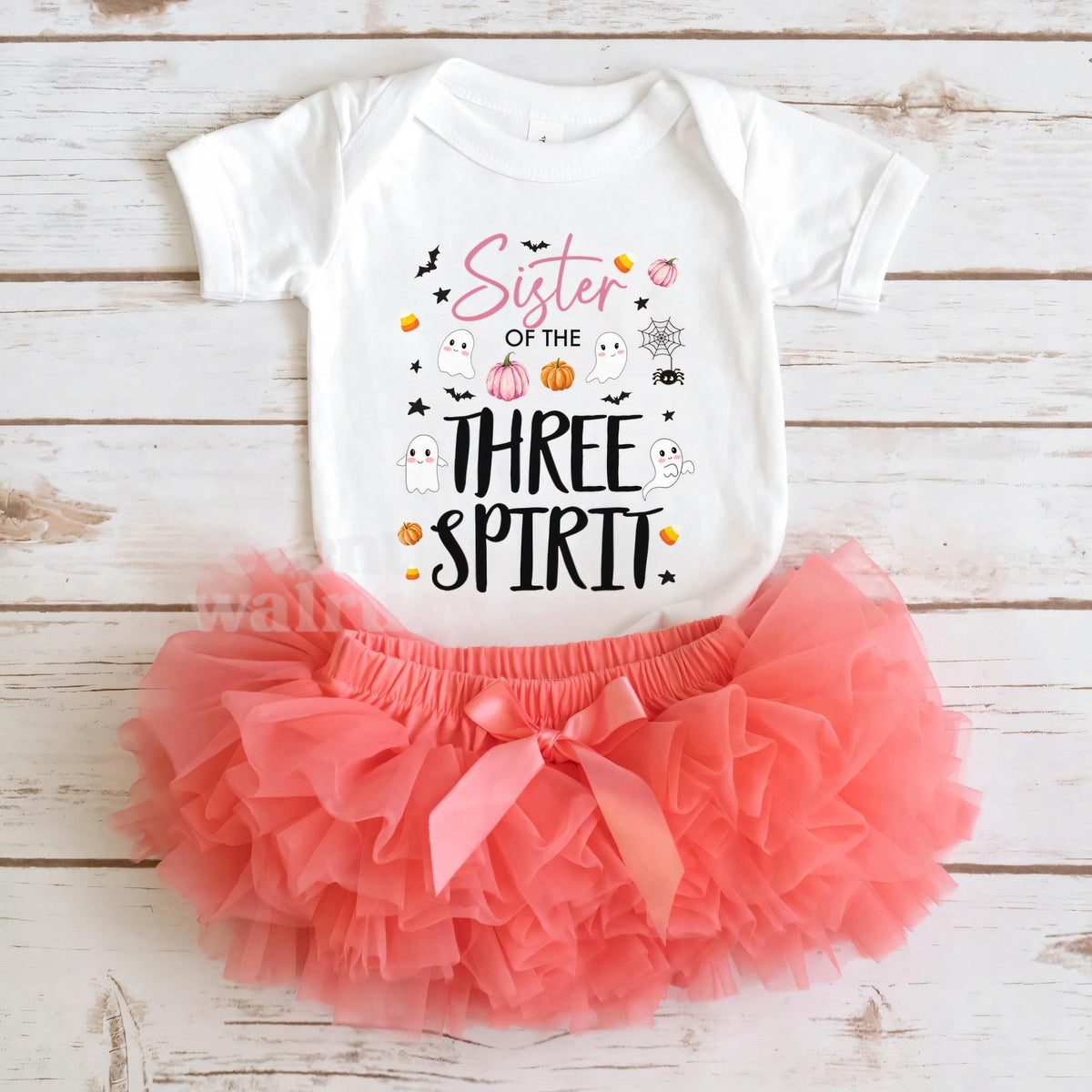 White Sister of the Three Spirit bodysuit laid flat with a coral tutu on whitewashed wood.