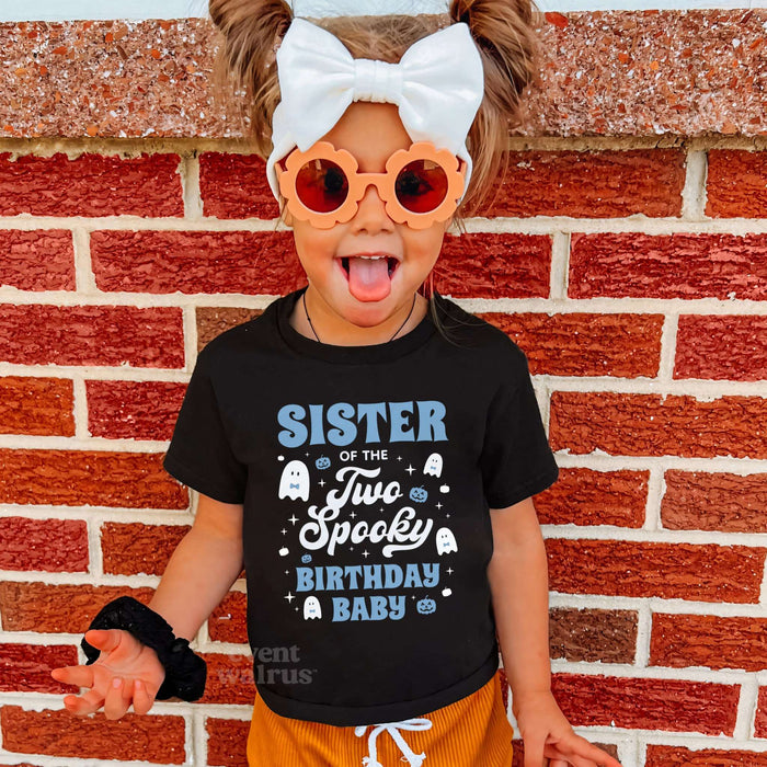 Girl in a big white bow wearing a black Sister of the Two Spooky shirt by a brick wall.