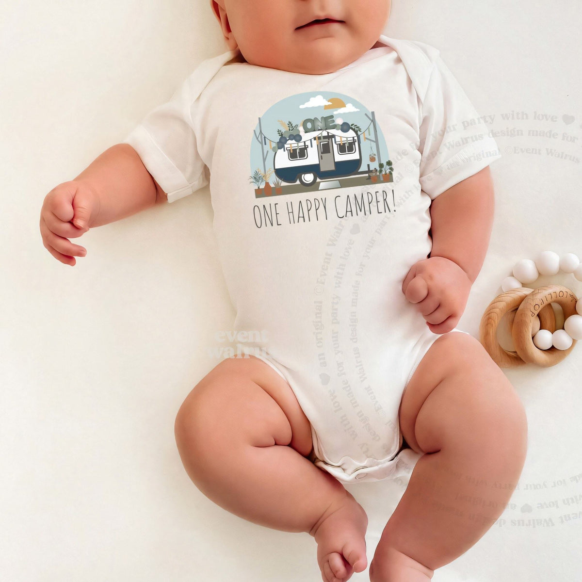 Baby lying on a white blanket in a white One Happy Camper bodysuit.