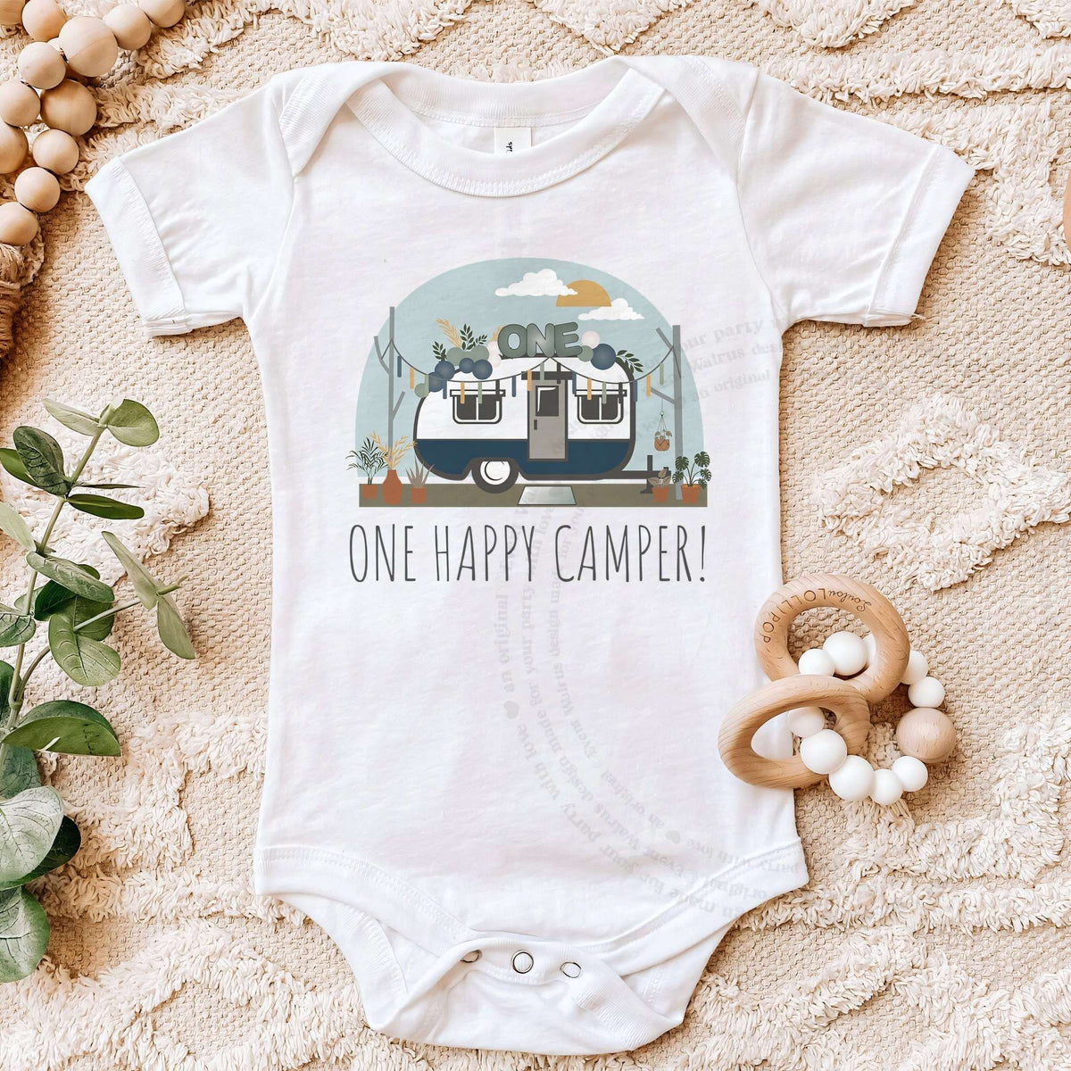 White One Happy Camper bodysuit on a beige blanket with a wooden teether.
