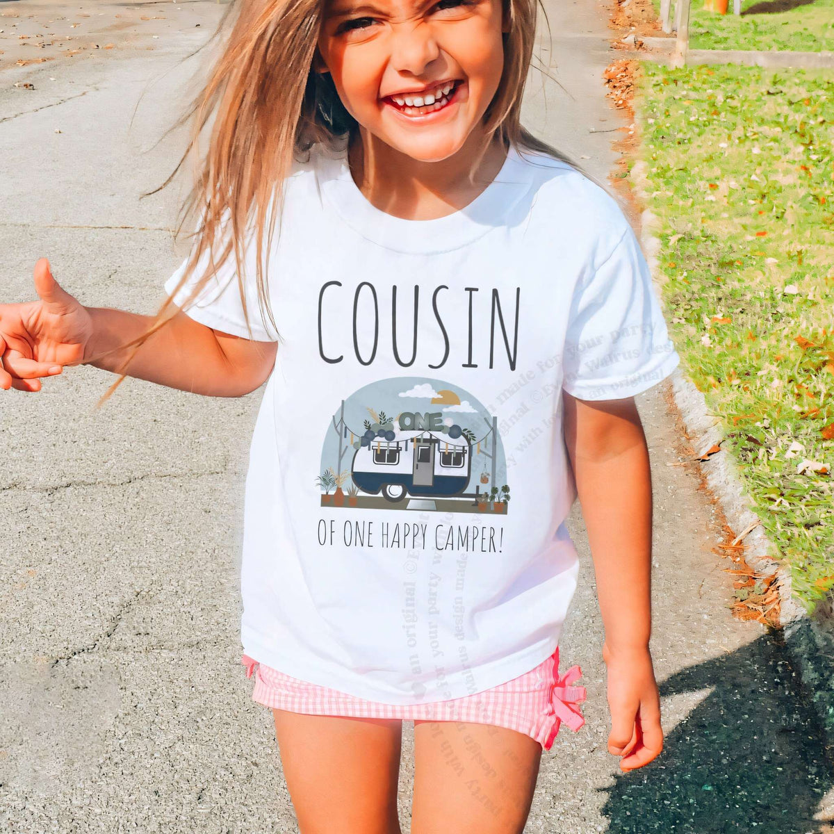 Laughing girl outdoors in a white Cousin of One Happy Camper kids tee.