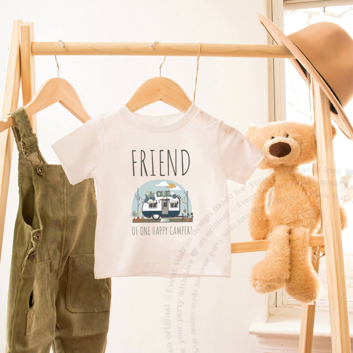 White Friend of One Happy Camper toddler tee on a wooden clothes rack beside a teddy bear.