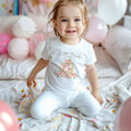 Smiling toddler girl among pink balloons in a white This Little Pumpkin Is Turning One tee.