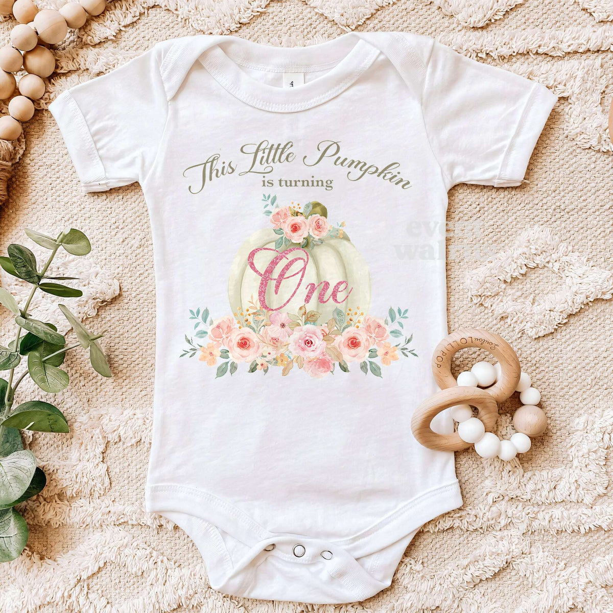 White Little Pumpkin bodysuit on a beige blanket with a wooden teether.