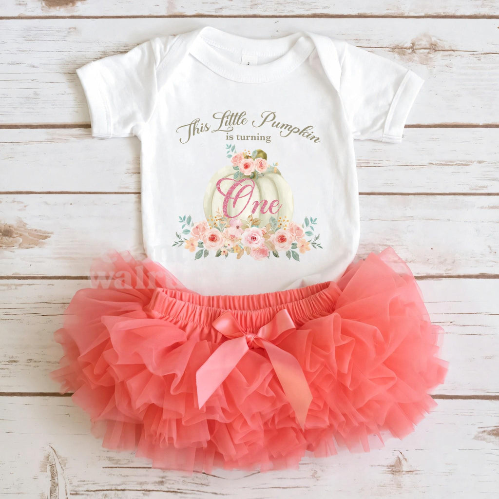 White Little Pumpkin bodysuit laid flat with a coral tutu on whitewashed wood.