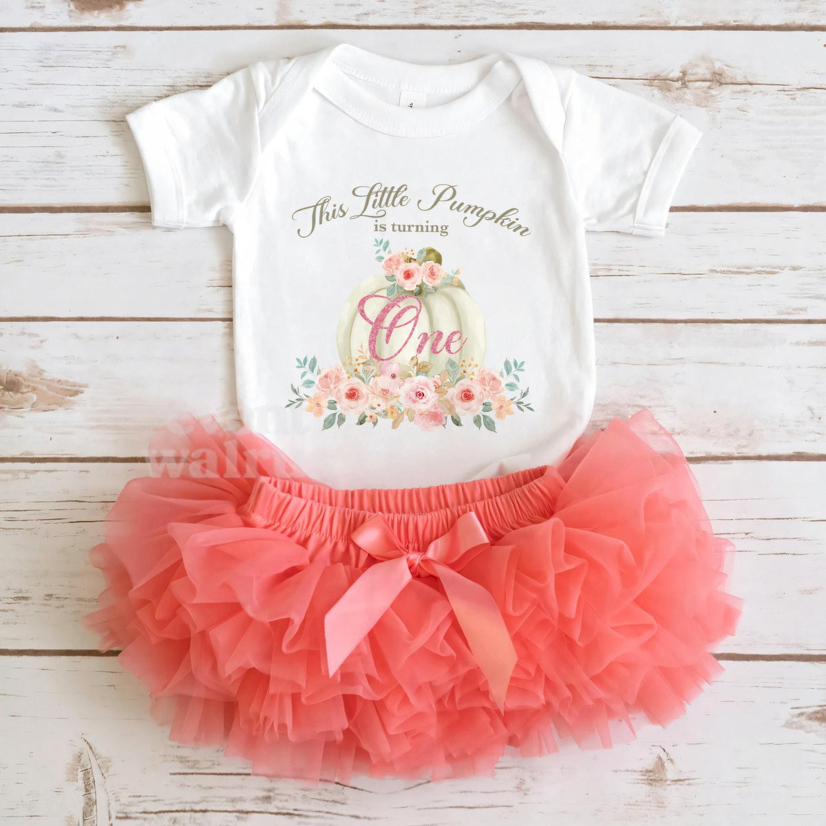 White Little Pumpkin bodysuit laid flat with a coral tutu on whitewashed wood.