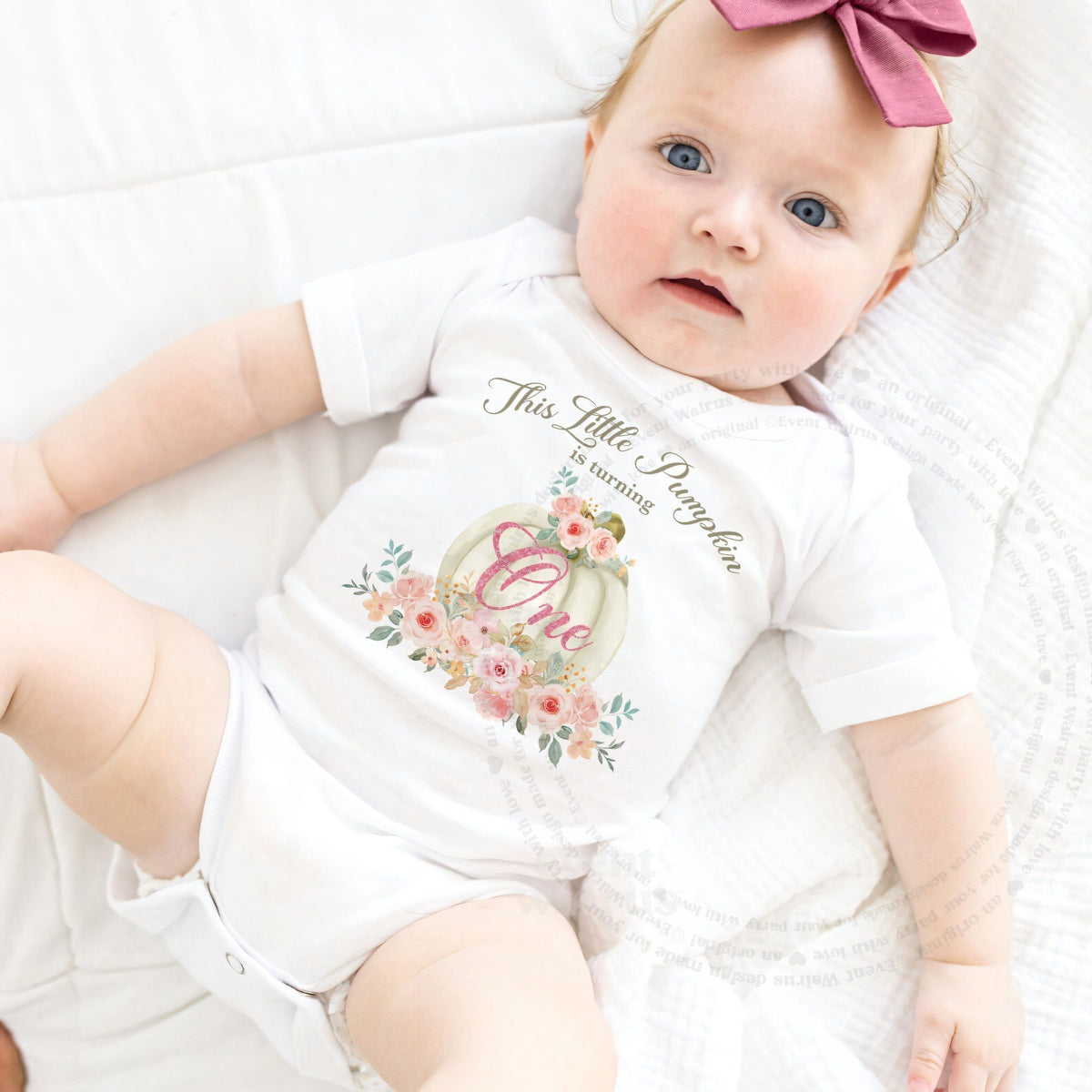Baby girl with a pink bow lying in a white This Little Pumpkin Is Turning One bodysuit.