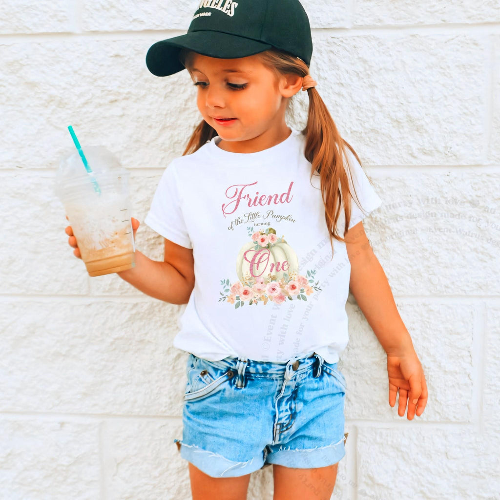 Girl in a ball cap holding a drink in a white Friend of the Little Pumpkin shirt.