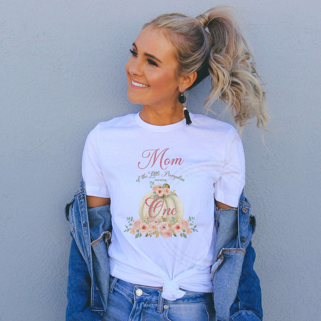 Smiling woman in a denim jacket wearing a white Mom of the Little Pumpkin shirt with a cream pumpkin.