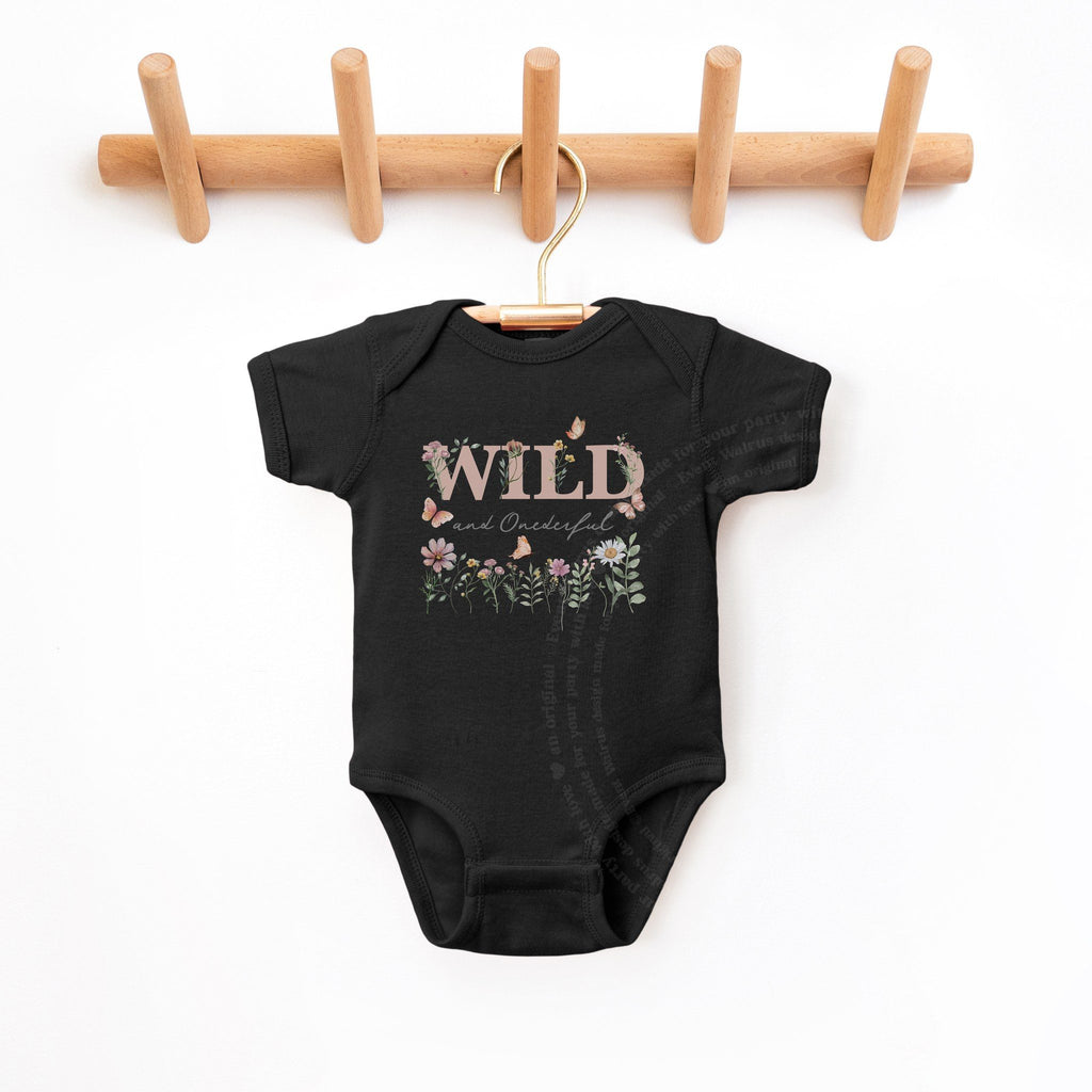 Black Wild and Onederful first birthday bodysuit hanging on a wooden peg rail.