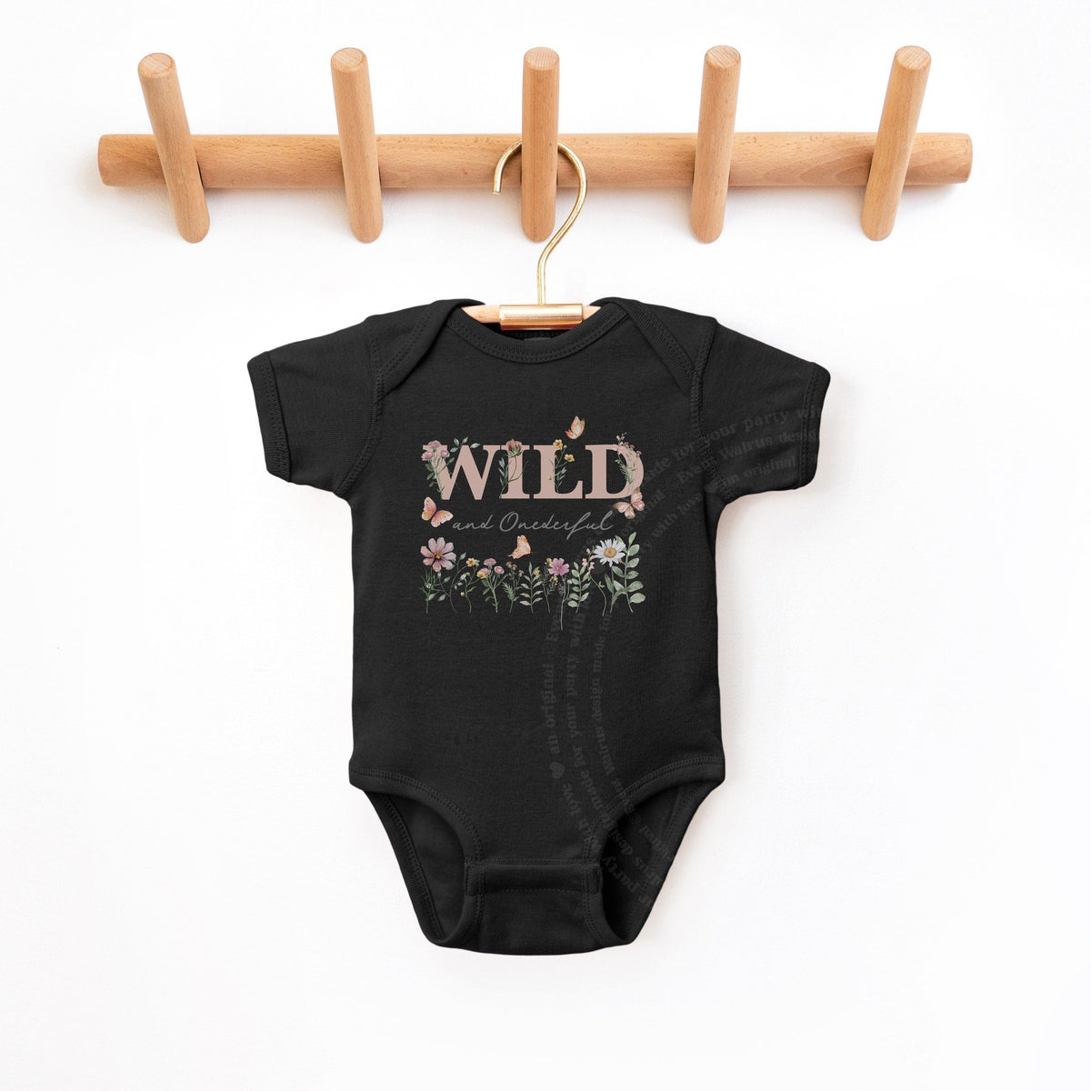 Black Wild and Onederful first birthday bodysuit hanging on a wooden peg rail.