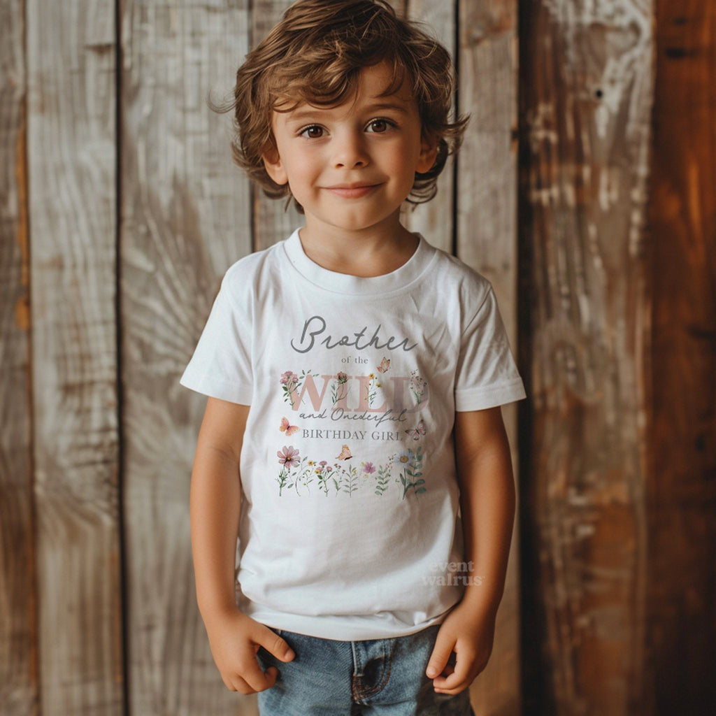 Toddler boy against a wood wall in a white Brother of the Wild and Onederful tee.