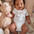 Smiling baby in a basket wearing a white Wild and Onederful bodysuit with pink wildflowers.