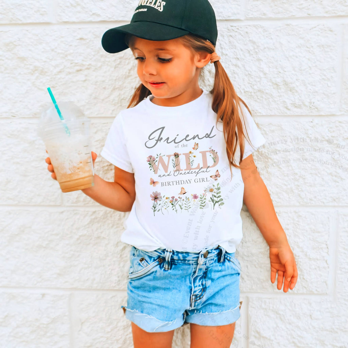 Girl in a ball cap holding a drink in a white Friend of the Wild and Onederful tee.