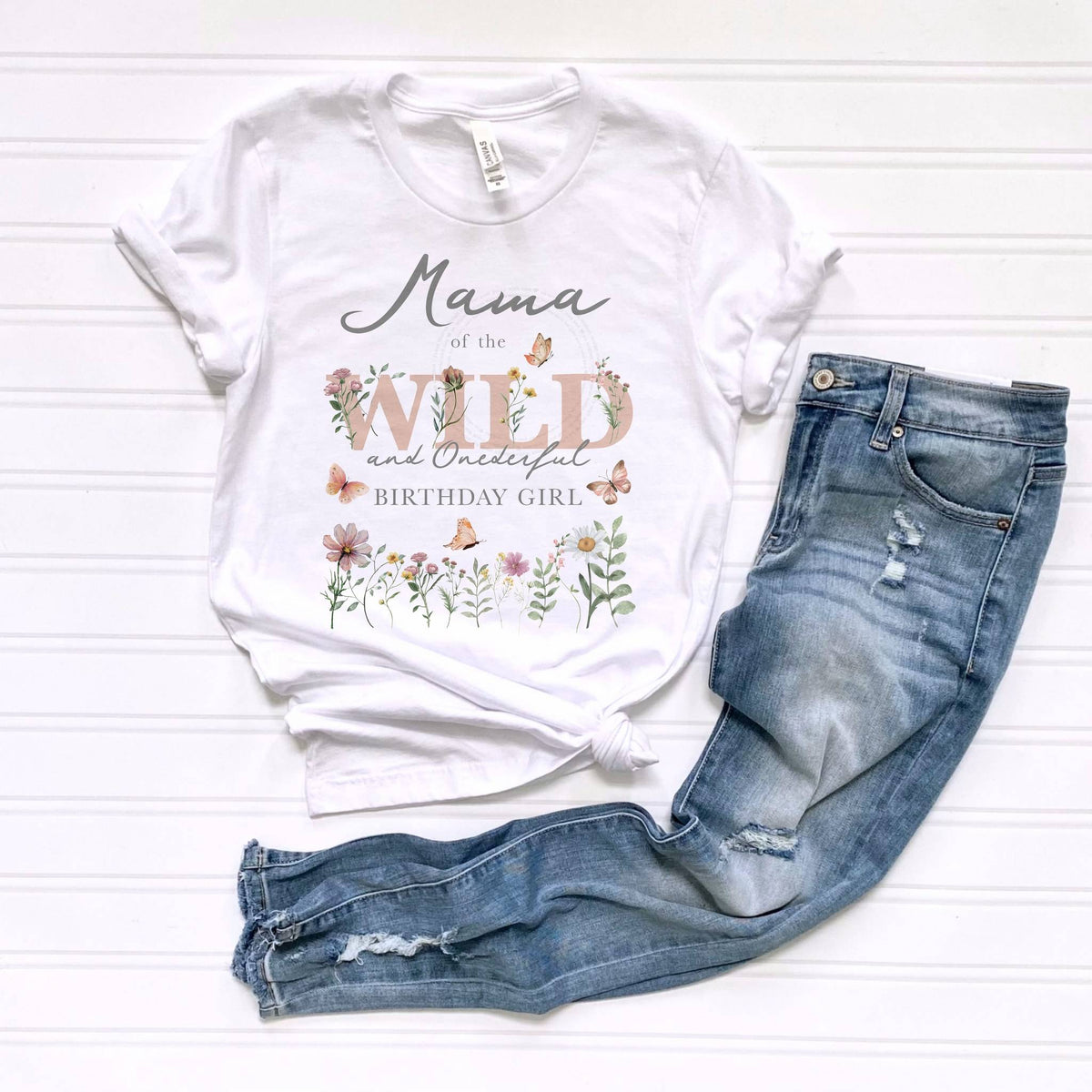 White Mama of the Wild and Onederful adult tee laid flat beside ripped jeans.