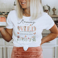 Mom holding a mug in a white Mommy of the Wild and Onederful Birthday Girl shirt with dusty pink wildflowers.