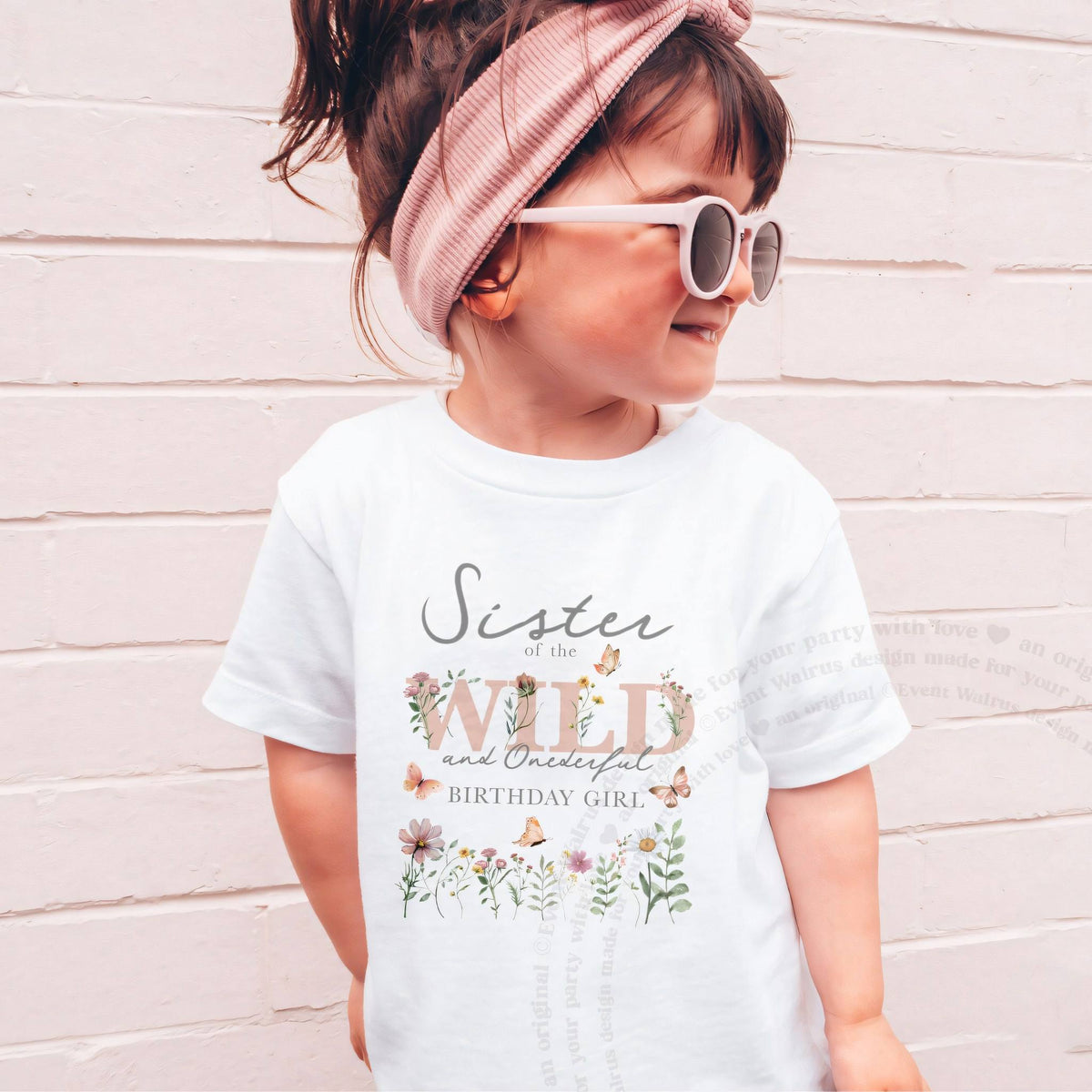 Girl in sunglasses and a pink headband wearing a white Sister of the Wild and Onederful kids tee.