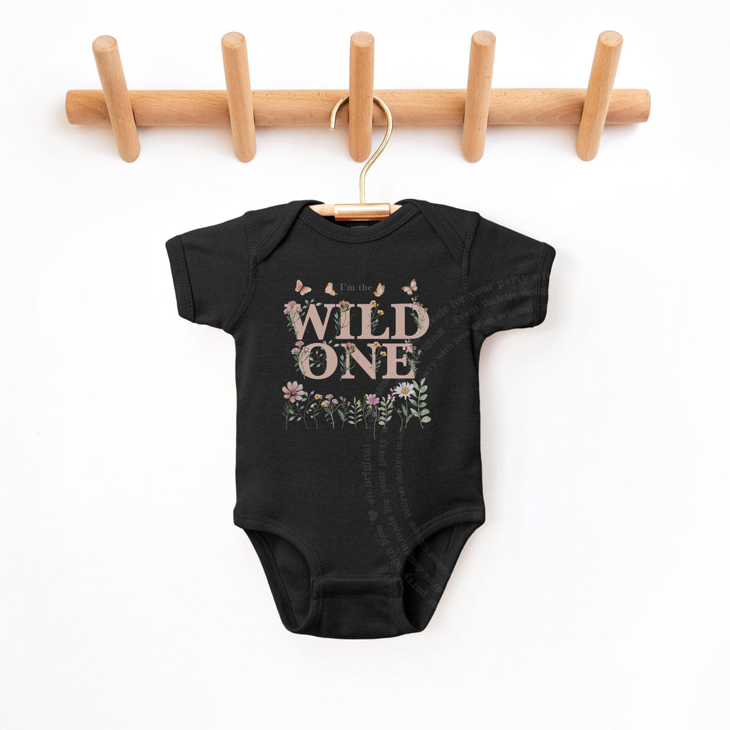Black I'm the Wild One baby bodysuit hanging on a wooden peg rail.