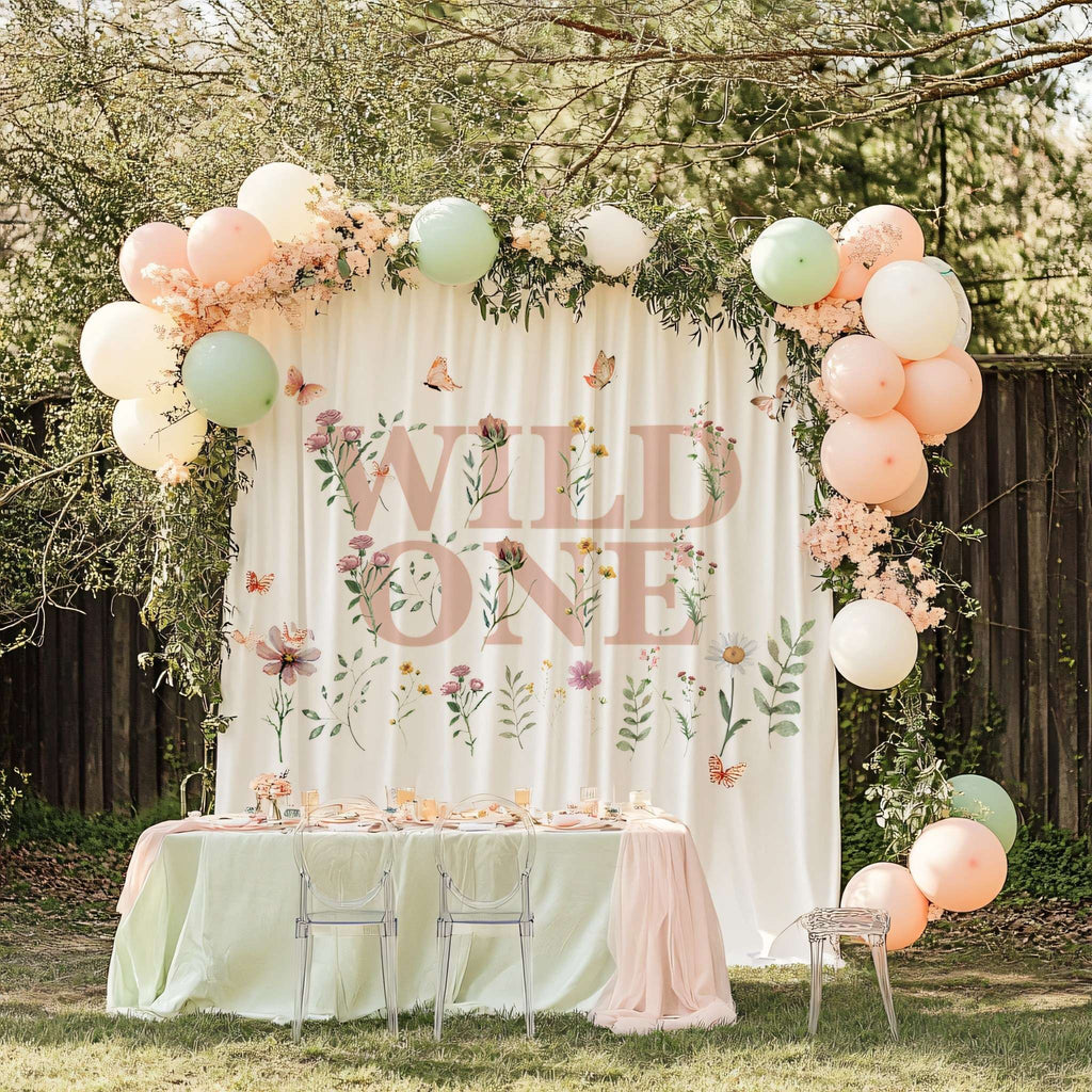 Pink Wild One backdrop behind a sage green party table with clear chairs and balloons on both sides.