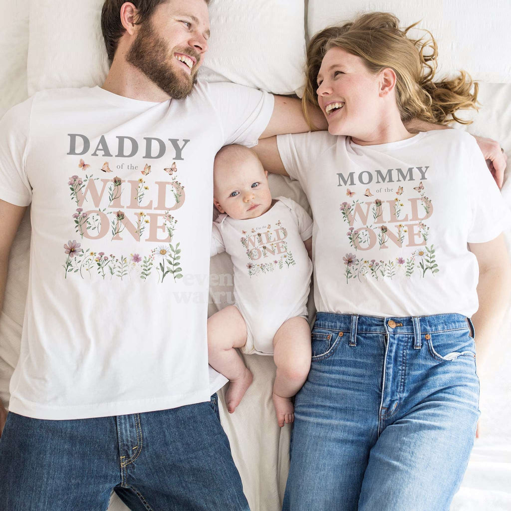 Dad, Mom and baby in matching white Daddy, Mommy and Wild One wildflower birthday shirts.