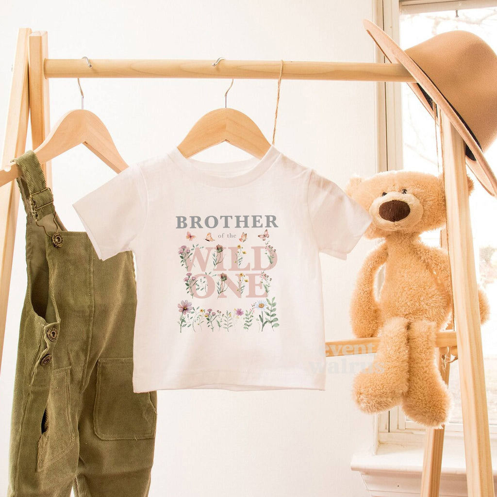 White Brother of the Wild One toddler tee hanging beside a teddy bear.