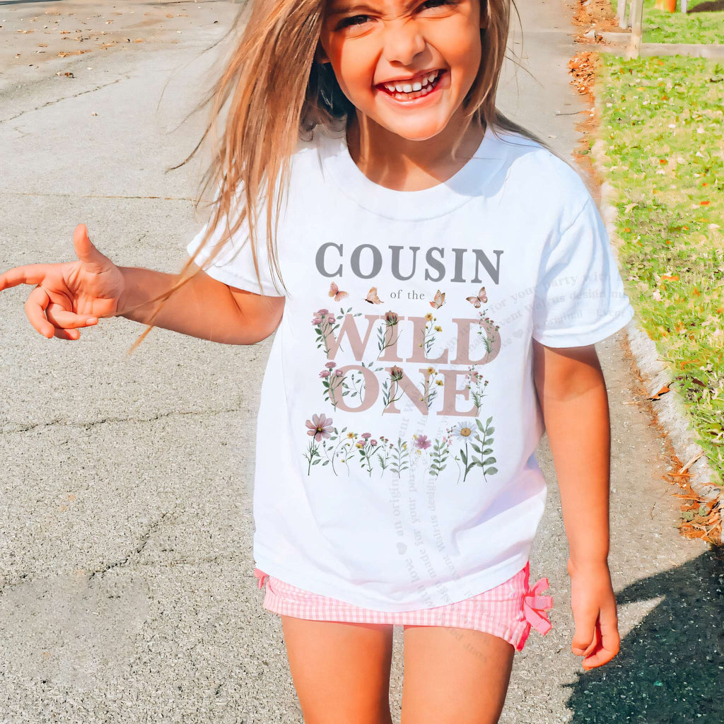 Smiling girl outdoors in a white Cousin of the Wild One wildflower tee and pink shorts.