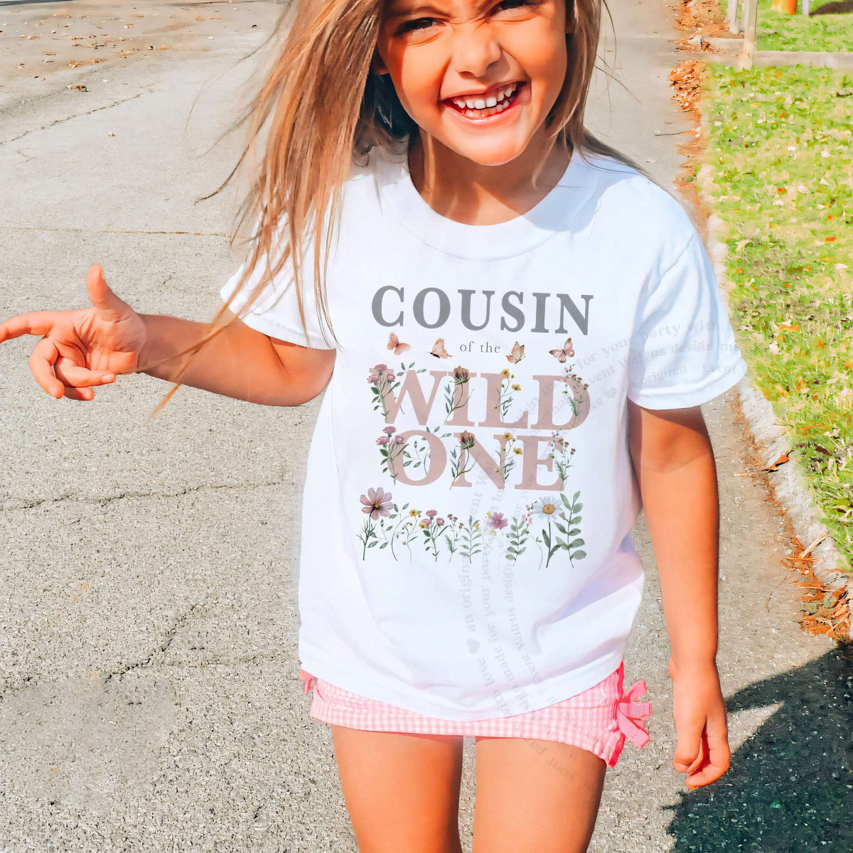 Smiling girl outdoors in a white Cousin of the Wild One wildflower tee and pink shorts.