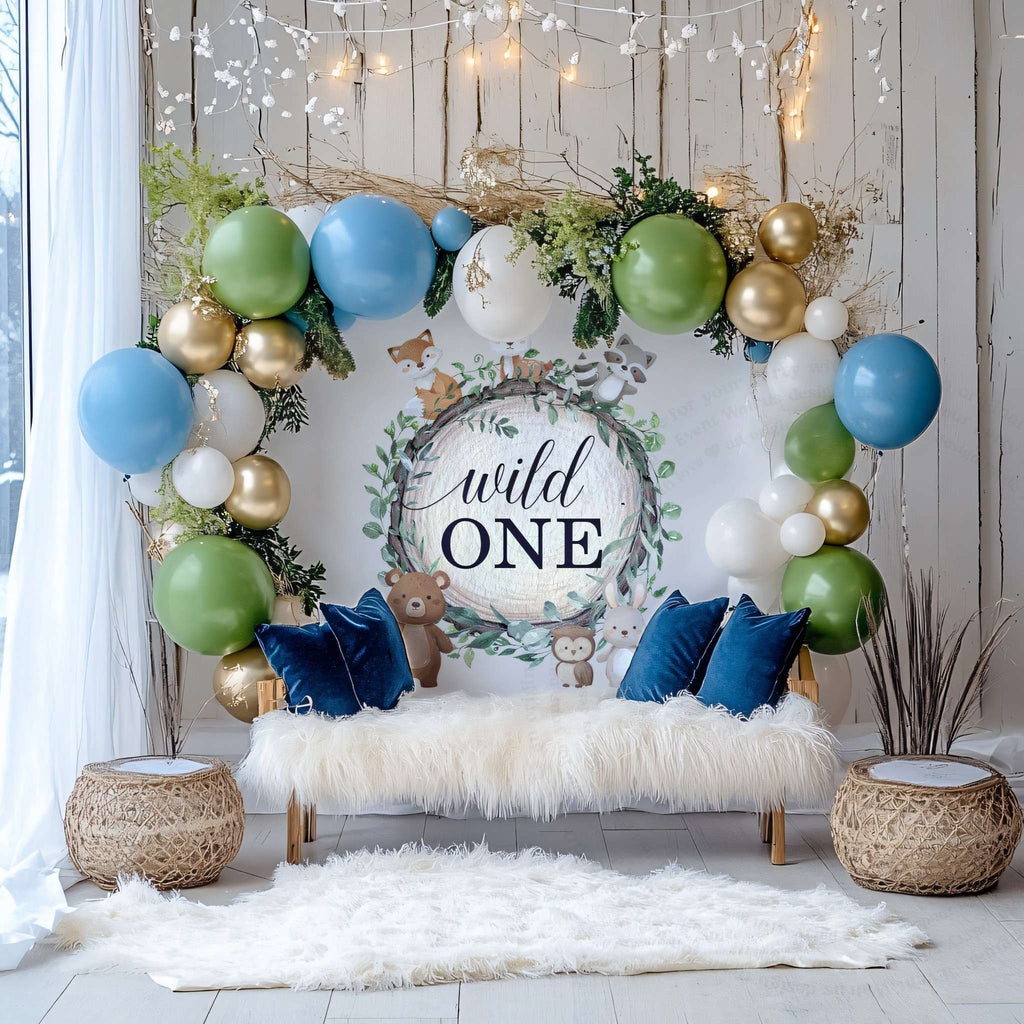 Woodland wild one backdrop behind a white fur bench with blue and green balloons and gold accents.