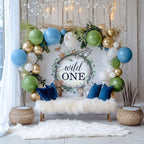 Woodland wild one backdrop behind a white fur bench with blue and green balloons and gold accents.