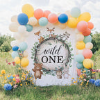 Wild one woodland backdrop in a grassy field with a bright balloon arch and wildflowers.