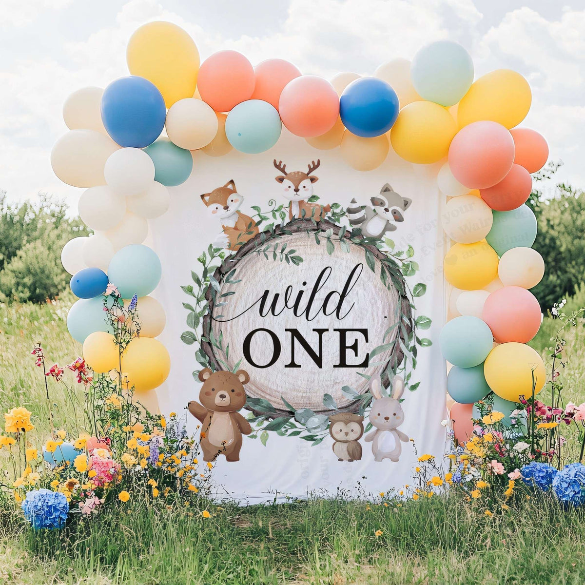 Wild one woodland backdrop in a grassy field with a bright balloon arch and wildflowers.