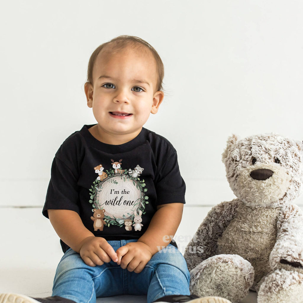 Smiling toddler beside a teddy bear in a black I'm the Wild One woodland tee.