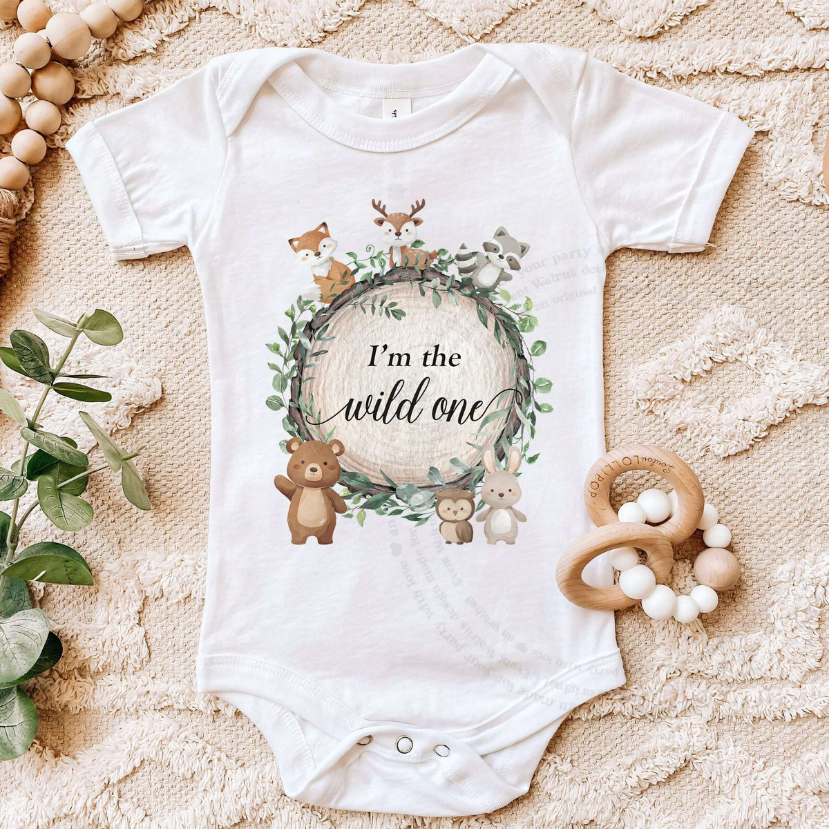 White I'm the Wild One bodysuit on a beige blanket with a wooden teether.