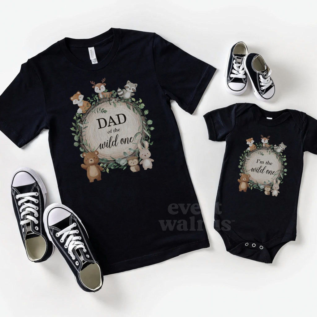 Black Dad of the Wild One shirt and a matching black baby bodysuit laid out with sneakers.